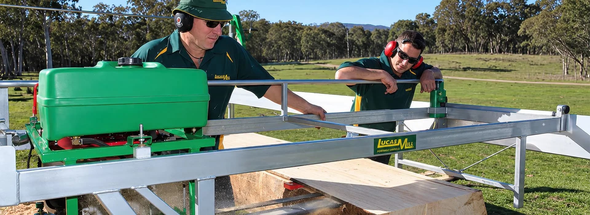 Two operators in ear protection running a Lucas Mill swing-blade sawmill over a freshly sawn beam
