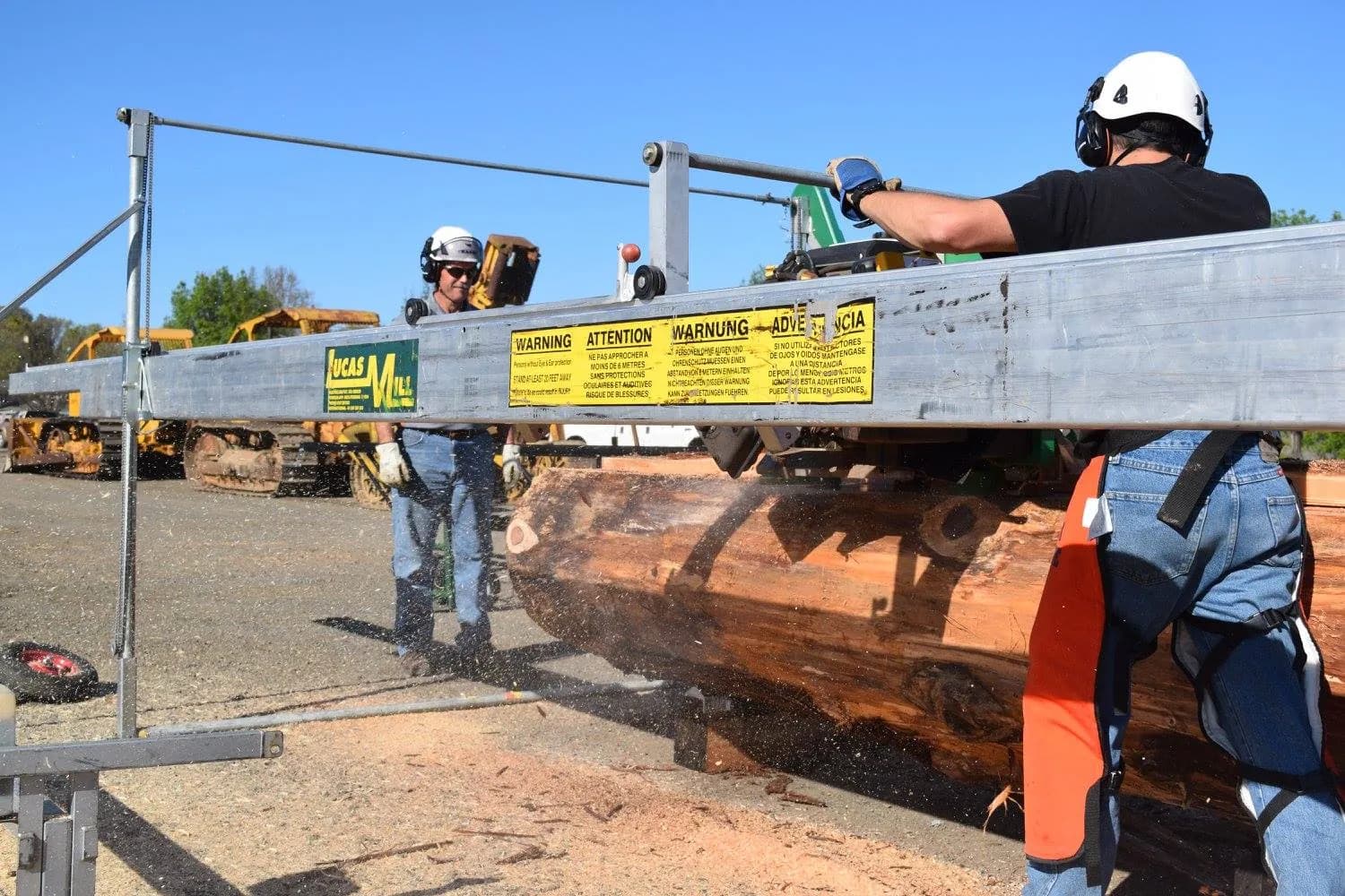 Two operators in hard hats cutting a large redwood log on a Lucas Mill at a Bailey's show