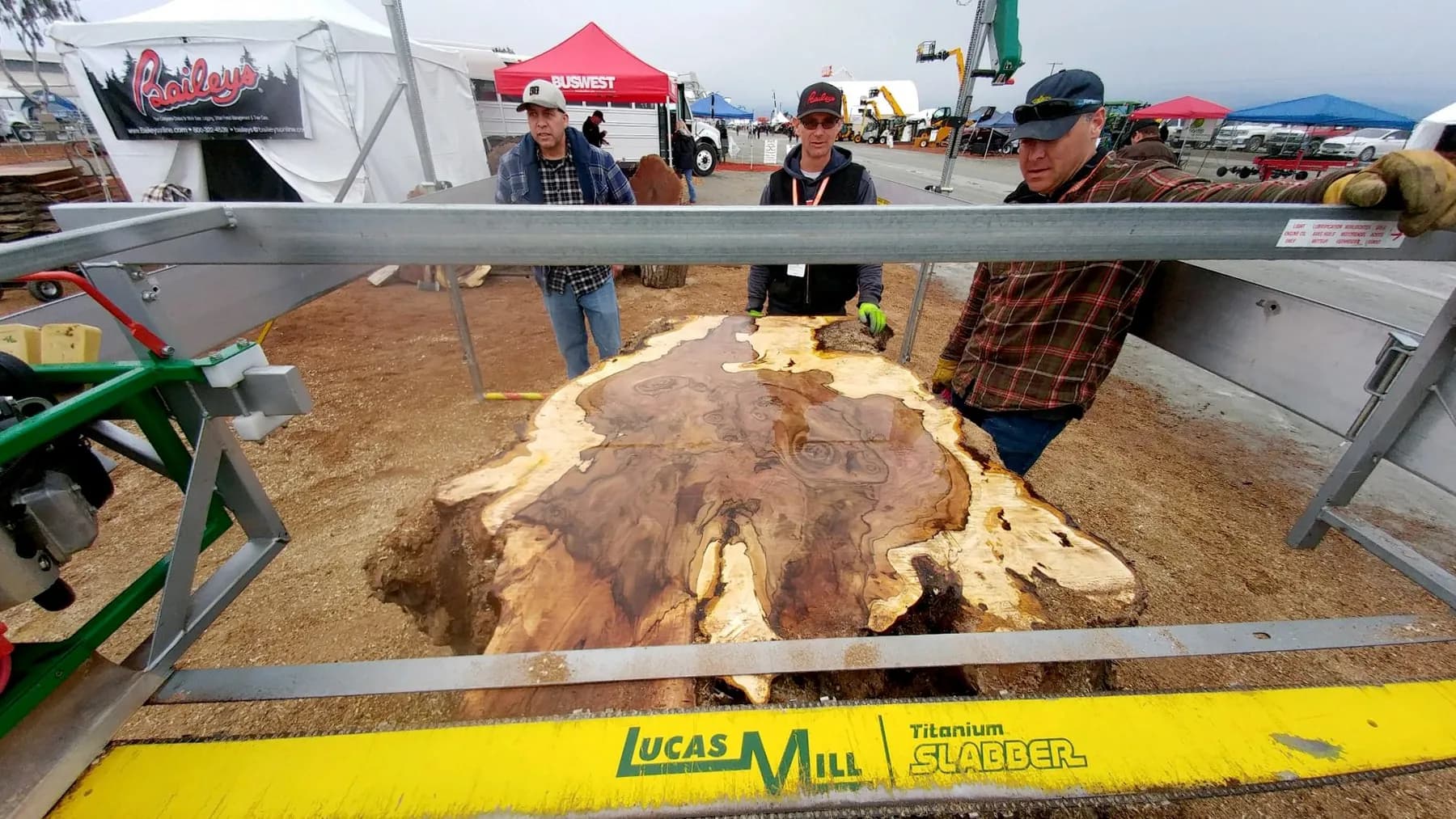 Lucas Mill slabber cutting a wide burl slab as visitors watch at a show