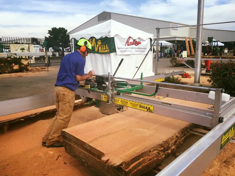 Operator at a Lucas Mill beside a wide fresh-cut slab, Bailey’s tent behind