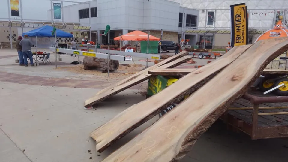 Long live-edge slabs leaning against a Lucas Mill at a show