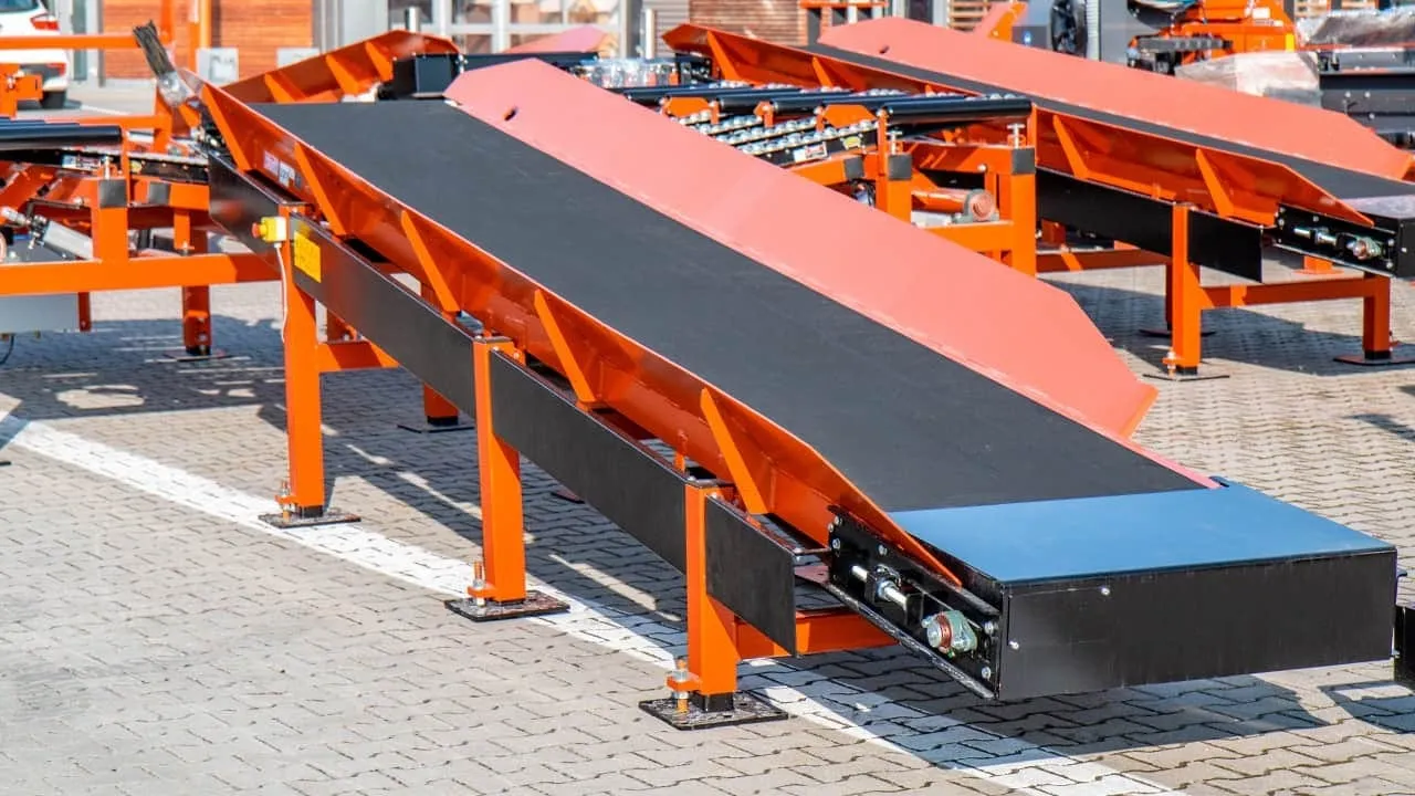 Wood-Mizer incline belt conveyor beside other conveyors on a paved yard