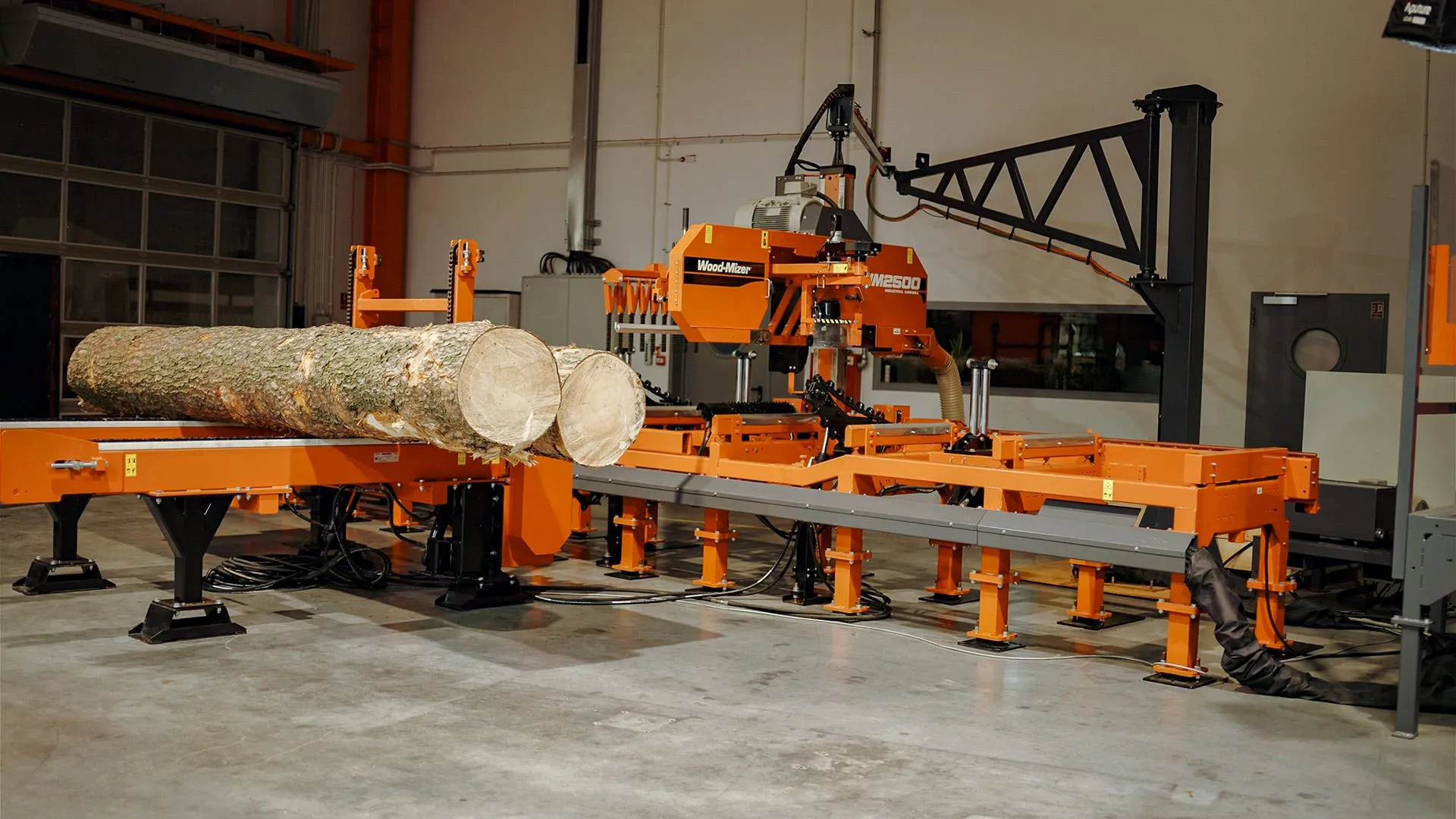 Wood-Mizer WM2500 industrial sawmill with two logs on the loading deck inside a workshop