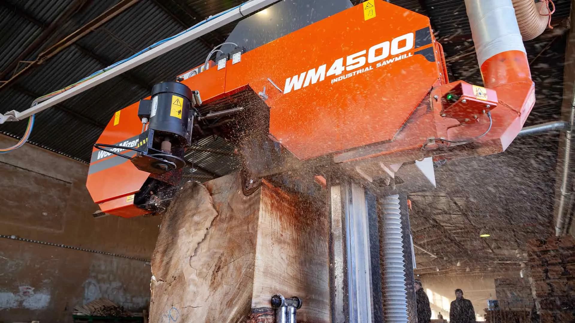 Wood-Mizer WM4500 industrial sawmill head sawing a large cant, sawdust in the air
